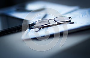 Eyeglasses lie on the documents and charts, next to the Tablet PC