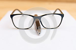 Eyeglasses lie on the handle in the shape of a nose, on a clean and white sheet of paper