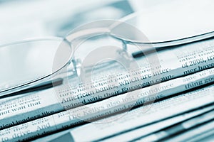 Eyeglasses lie on a pile of newspapers.Blue toned