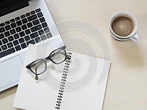 Eyeglasses on notebook, laptop computer and a cup of hot coffee