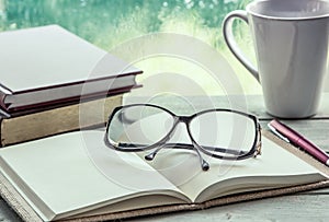 Eyeglasses on open notebook with book,pen and coffee cup