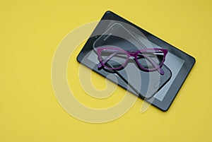 Eyeglasses over Tablet and Mobile Phone over Yellow Background with copy space. Education, technoogy, internet.