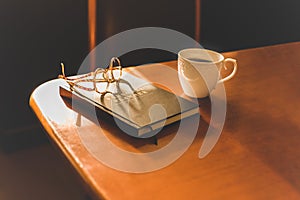 Eyeglasses placed on notebooks with coffee mug on table with golden sunlight.