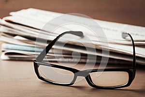 Eyeglasses and stack of newspapers on wooden desk for themes of ophthalmology, poor vision and reading