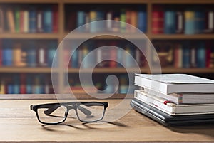 Eyeglasses and stacked books with laptop on wooden desk in home office room