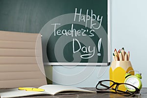 Eyeglasses and stationery on grey table near chalkboard with inscription HAPPY TEACHER`S DAY