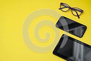 Eyeglasses on Tablet and Mobile Phone over Yellow Background with copy space. Education, technoogy, internet.