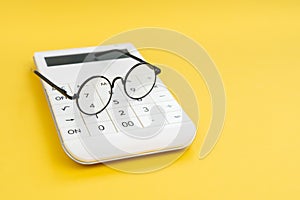 Eyeglasses on white calculator on yellow background with copy space using as analyze numbers or data, forecast or foresee result