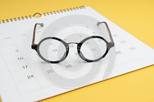 Eyeglasses on white clean calendar on yellow background using as thinking about plan, schedule or meeting apointment concept
