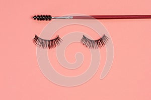 Eyelash extension, concept. Women`s eyelashes and brush for styling and combing eyebrows on a pink background