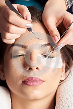 Eyelash Extension Procedure. Close-up hands beautician with tweezers in hands