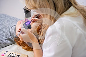 Eyelash extension procedure using ultraviolet lamp in modern beauty salon. Innovative lash enhancement technology with photo