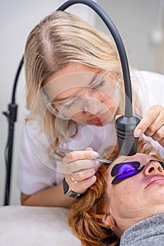 Eyelash extension procedure using ultraviolet lamp in modern beauty salon. Innovative lash enhancement technology with photo