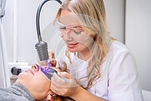 Eyelash extension procedure using ultraviolet lamp in modern beauty salon. Innovative lash enhancement technology with photo