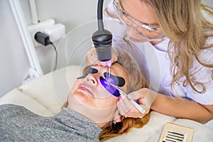 Eyelash extension procedure using ultraviolet lamp in modern beauty salon. Innovative lash enhancement technology with photo