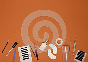 Eyelash extension tools on an orange background, free space for text, top view. Artificial eyelashes, tweezers, microbrushes,