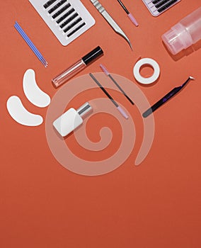 Eyelash extension tools on an orange background, free space for text, top view. Artificial eyelashes, tweezers, microbrushes,