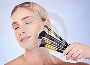 Eyes closed, face and makeup of woman with brushes in studio isolated on a blue background. Facial cosmetics, beauty