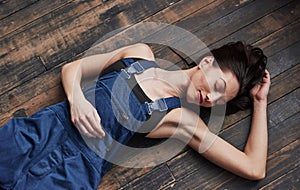 With eyes closed. Girl in the blue uniform for the work is lying on wooden floor having relax