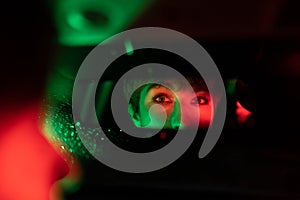 Eyes of European woman are reflected in automotive mirror riding taxi in evening rainy weather