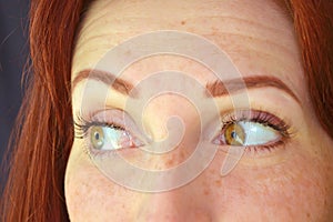 Eyes of girl with red hair and green eyes with eyelash extensions on a dark background looks emotionally