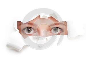 Eyes of woman peeking through a hole torn in white paper poster