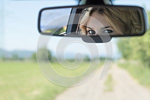 The eyes of the young driver woman are reflected in the rearview mirror.