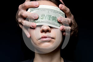 The eyes of a young woman are closed by a hundred-dollar bill. Money is blinding