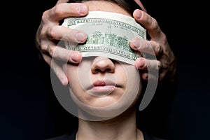 The eyes of a young woman are closed by a hundred-dollar bill. Money is blinding photo