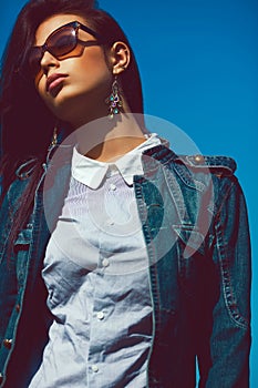 Eyewear concept. Fashion portrait of stylish brunette in trendy sunglasses and jeans jacket. Luxurious vintage earrings. Urban