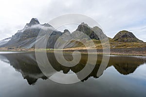 Eystrahorn mountain peaks with fog around and beautiful reflections in the calm lake.