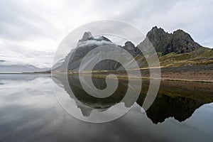 Eystrahorn mountain peaks are reflecting in the calm water on the south coast of Iceland.