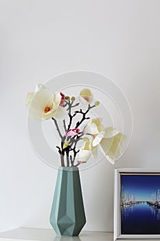 fabric magnolia in a decorative vase against a white background, next to it one of my pictures in the harbour of Heiligenhafen in