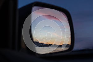 A fabulous beautiful pink sunset reflected in the mirror of a distant view of the car on Lake Baikal in winter.