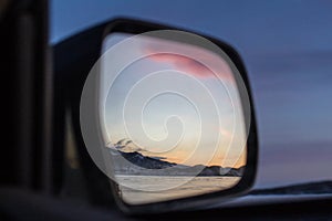 A fabulous beautiful pink sunset reflected in the mirror of a distant view of the car on Lake Baikal in winter.