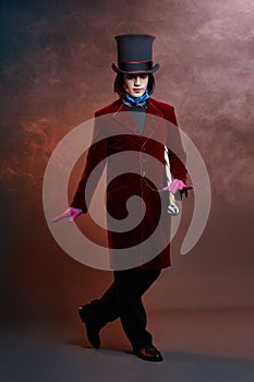 Fabulous circus man in a hat and a red suit posing in the smoke on a colored dark background. A clown at a party, man gentleman