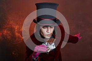 Fabulous circus man in a hat and a red suit posing in the smoke on a colored dark background. A clown at a party, man gentleman