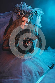 Fabulous creature, queen, sorceress, in a colorful suit and sword. Woman, model after 60, in the studio, dark background