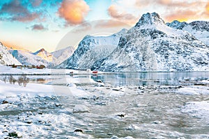 Fabulous frozen Flakstadpollen and Boosen fjords with cracks on ice during sunrise with Hustinden mountain on background on photo