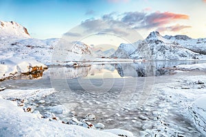 Fabulous frozen Flakstadpollen and Boosen fjords with cracks on ice during sunrise with Hustinden mountain on background on photo