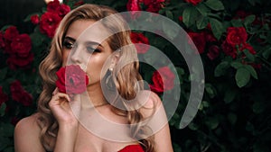 Fabulous girl with red lips in red dress on awesome summer roses background. Fantasy woman portrait. Awesome blonde