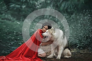 Fabulous image, dark-haired brunette attractive lady in short white dress, long red scarlet cloak lying on ground sits