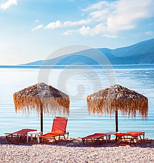 Fabulous landscape with umbrellas and orange sun beds on the seafront on Antisamos Beach on a sunny day on the coast of the Ionian