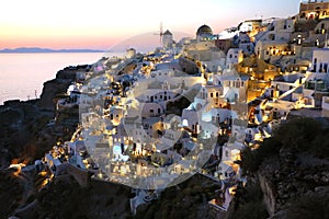 Fabulous picturesque village of Oia built on the rocks with traditional white houses and windmills in Santorini island at sunset