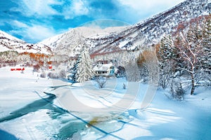 Fabulous winter scenery with frozen river with wooden houses and snow covered pine trees near Valberg village at Lofotens