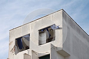 Facade of an abandoned building with collapsed window and broken blue curtains