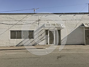 Facade of abandoned white washed building from outside with shadows and blue sky on a sunny day with copy space