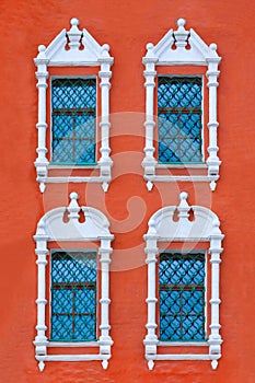 Facade of ancient red building with four windows with carved white stone platbands as texture vertical