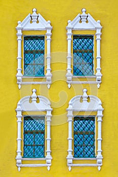 A facade of ancient yellow building with four windows with carved white stone platbands  as texture vertical