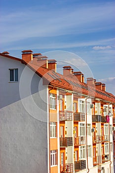 Facade of apartment building with terracotta tile roof shingles against blue sky